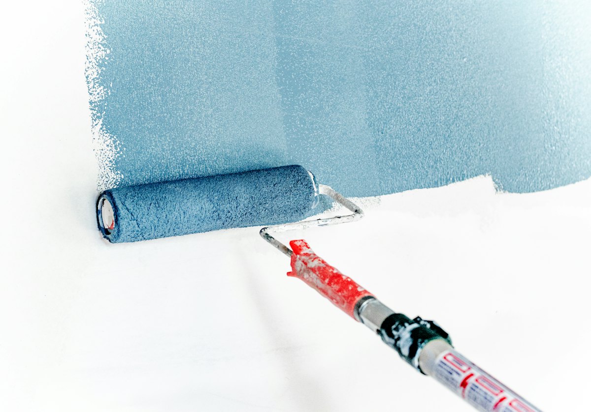 Paint roller laying a smooth blue coat on a white surface — the coating action behind a freshly painted timber fence